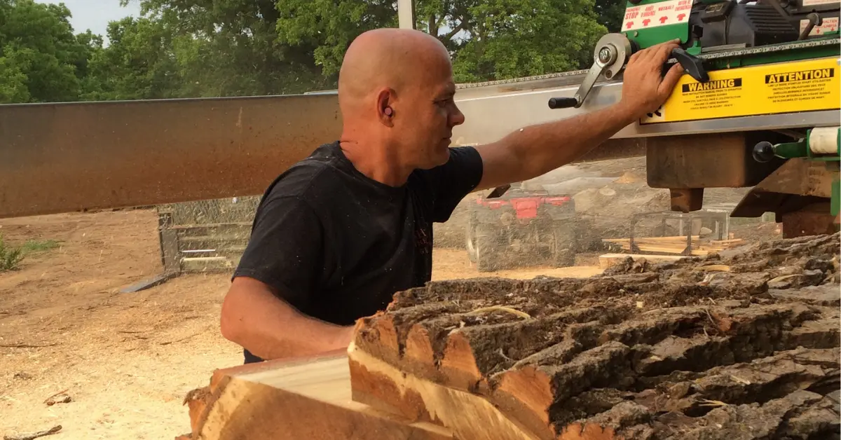 A Sharpe Tree Service worker adjusting the wood processing machine at an outdoor saw milling job site, with logs staged ready to be milled.